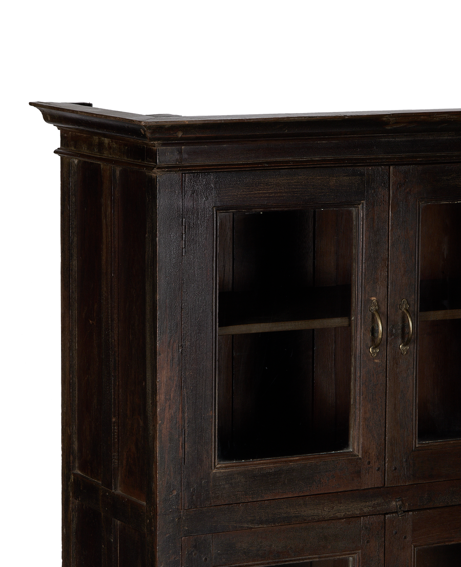 Close-up of vintage Indian oak wood cabinet with glass doors and brass handles.