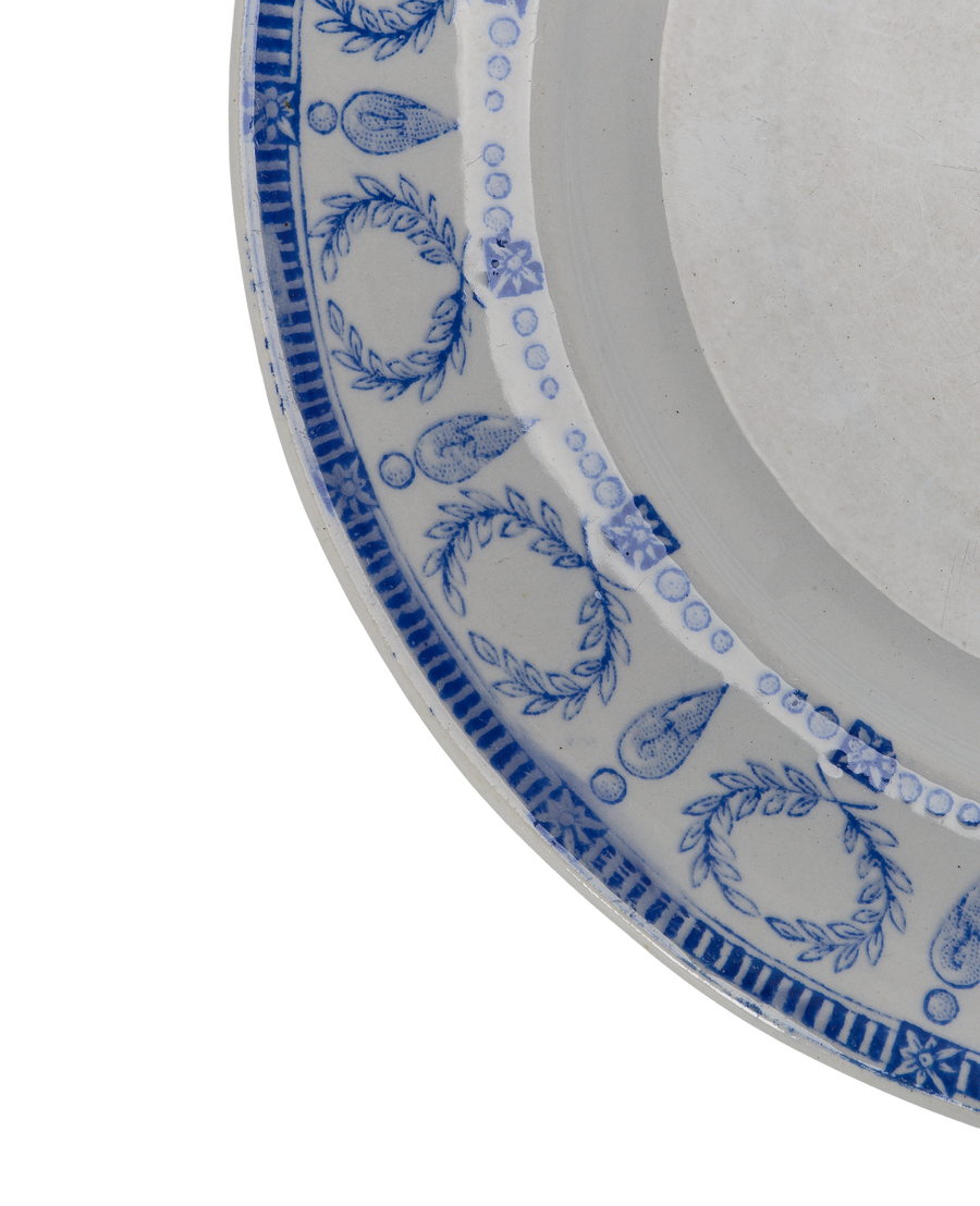 Close-up of vintage French blue motif plate rim, showcasing detailed floral and laurel wreath patterns.