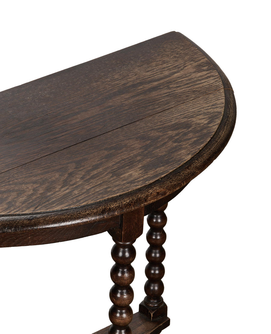 Vintage French oak demilune bobbin table showing distressed wood grain and turned legs.