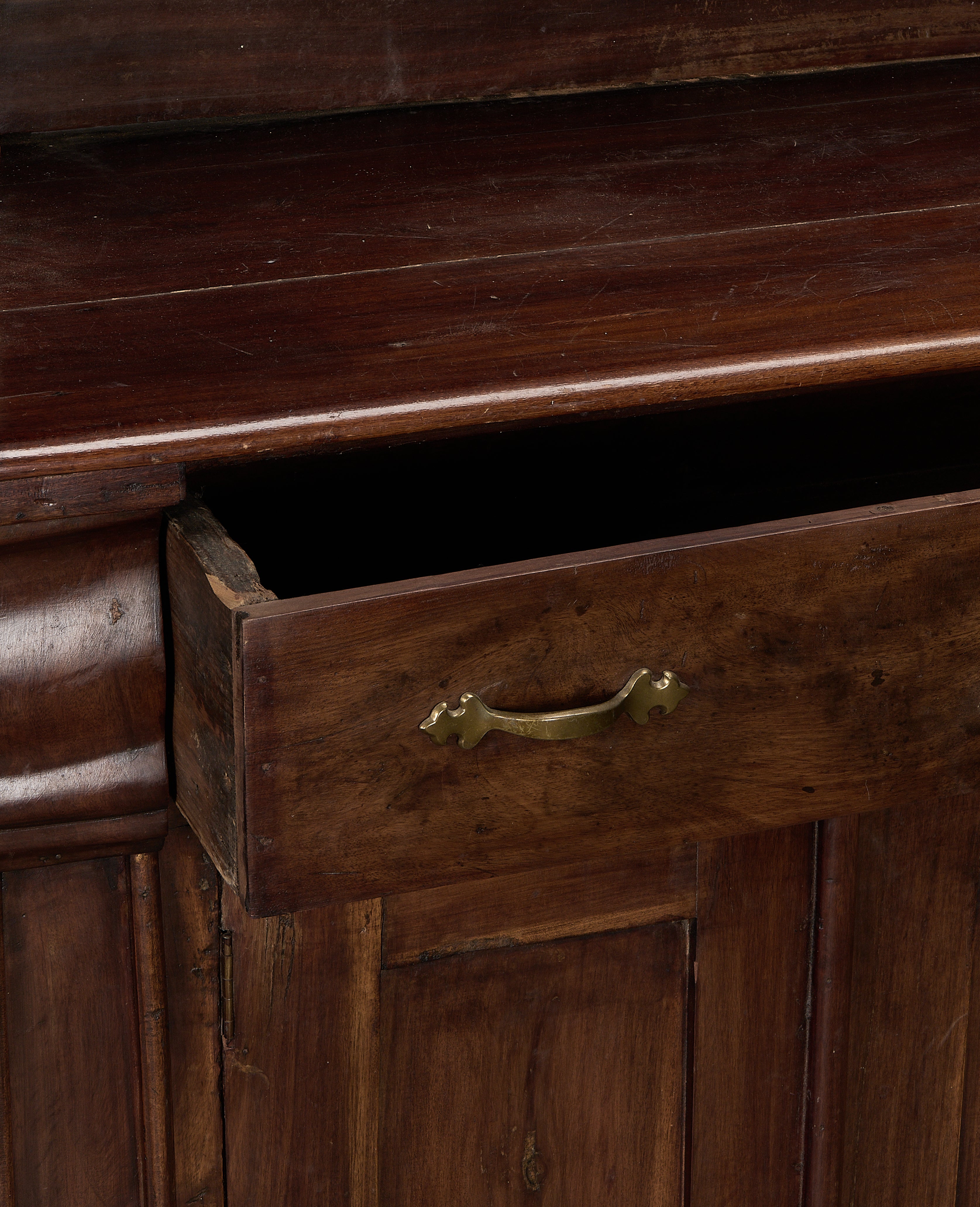 Open drawer of vintage French oak hutch, brass pull, dark wood interior.