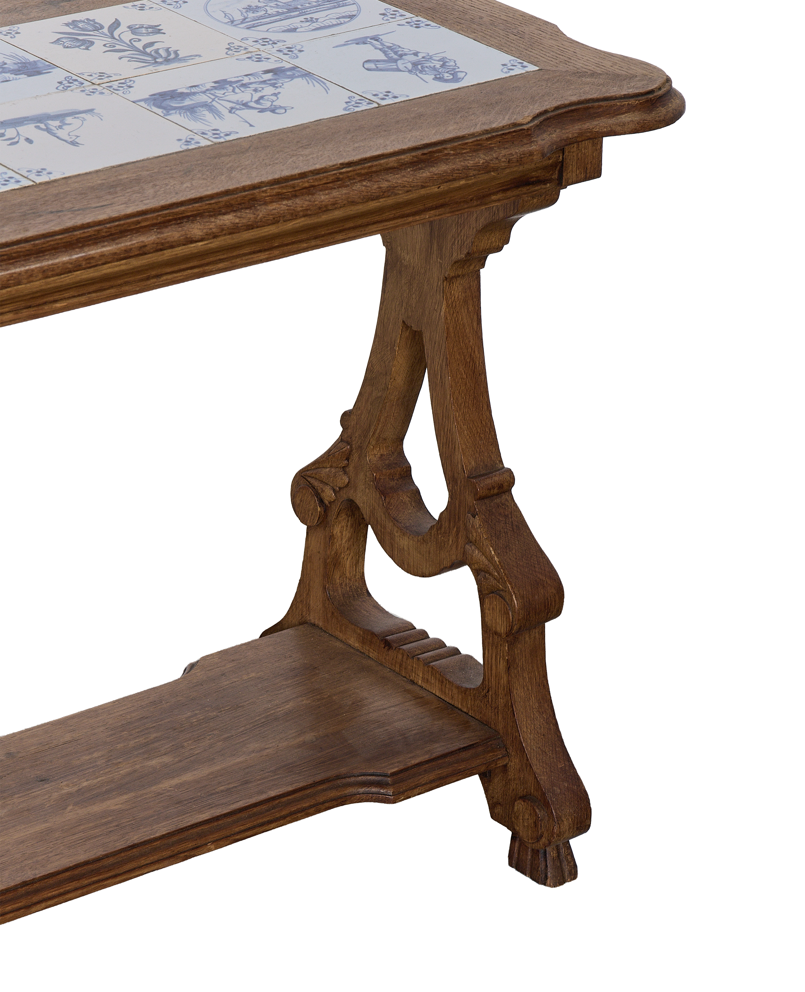 Vintage French oak table with Delft tile top, showing detailed carved legs and lower shelf.