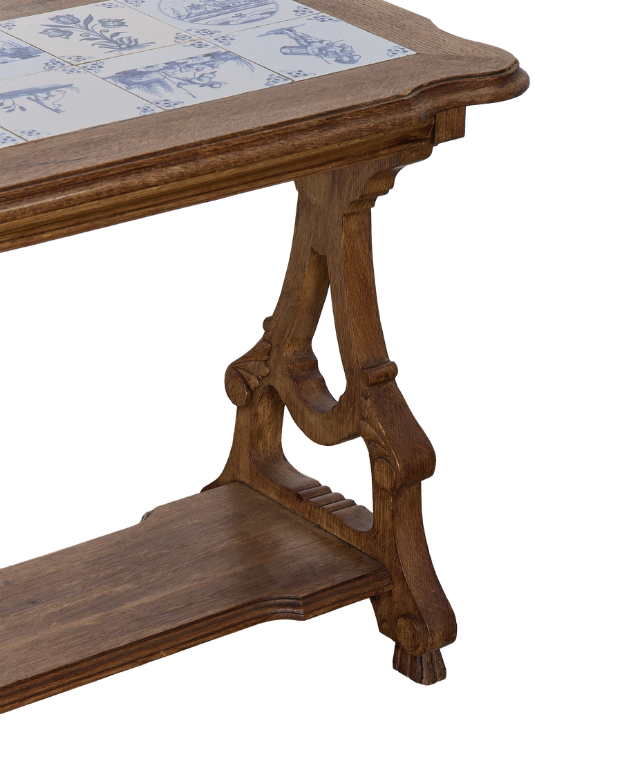 Vintage French oak table with Delft tile top, showing detailed carved legs and lower shelf.