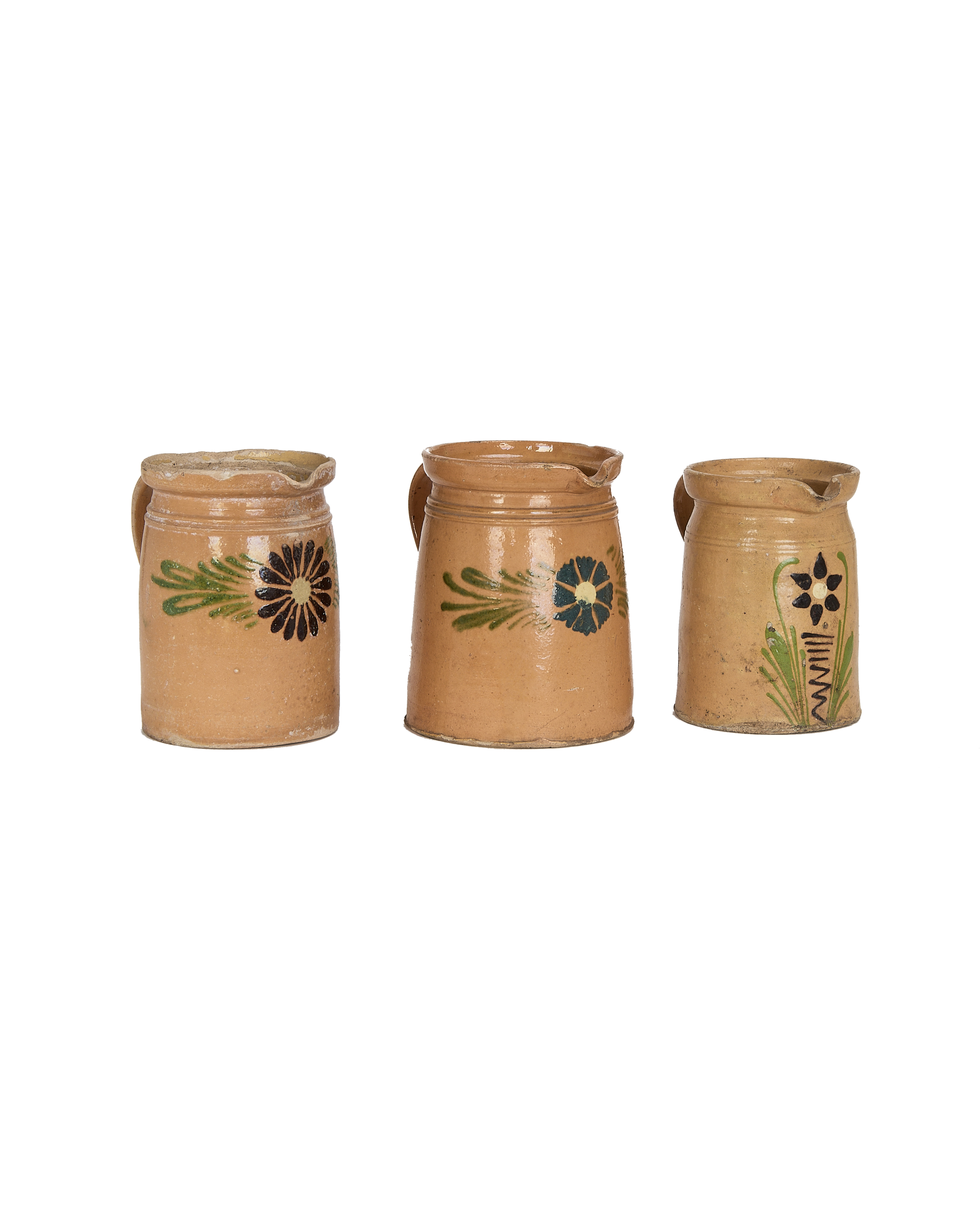 Three vintage French ceramic pitchers with mustard Alsace glaze and assorted floral details.
