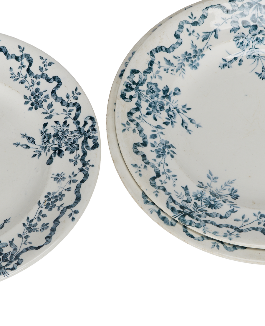 Close-up of vintage French ceramic wreath plates, showcasing intricate blue floral ribbon pattern details.
