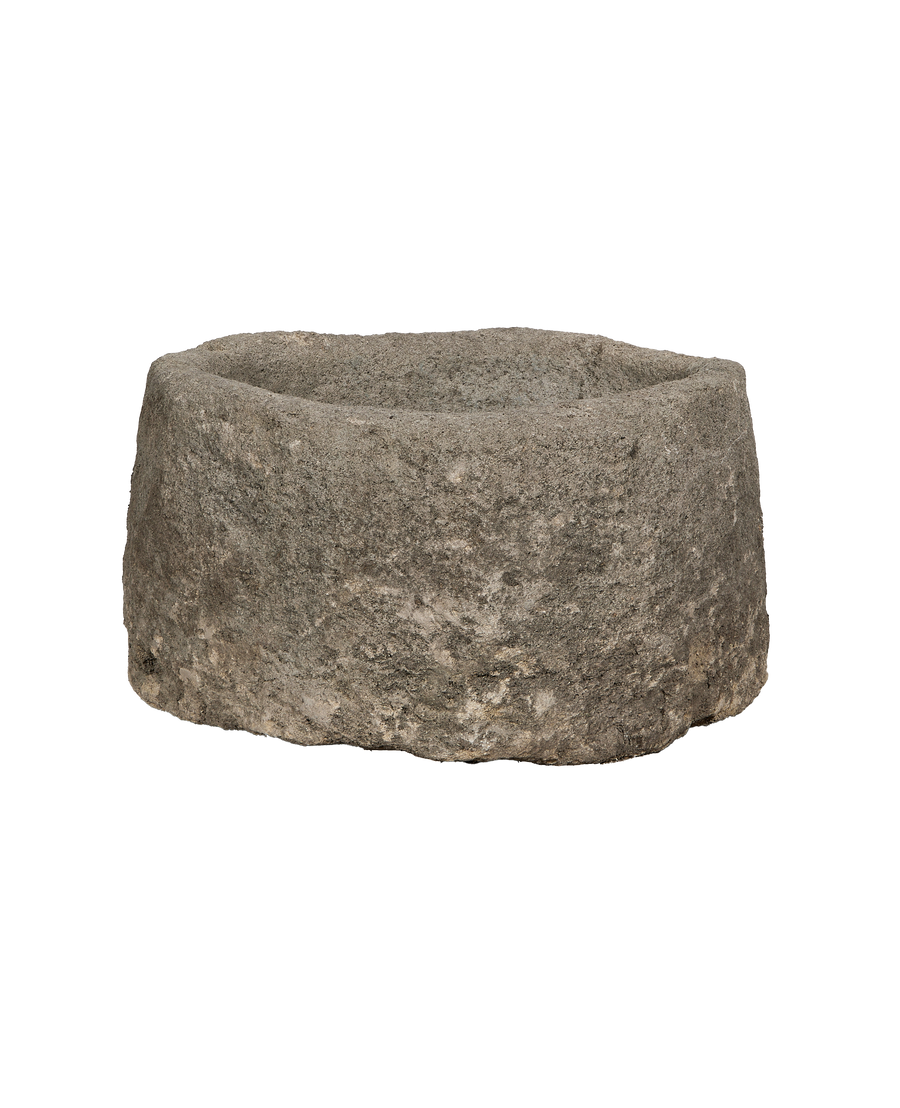 Vintage Indonesian round limestone trough, showing rugged texture and weathered gray stone from a side angle.
