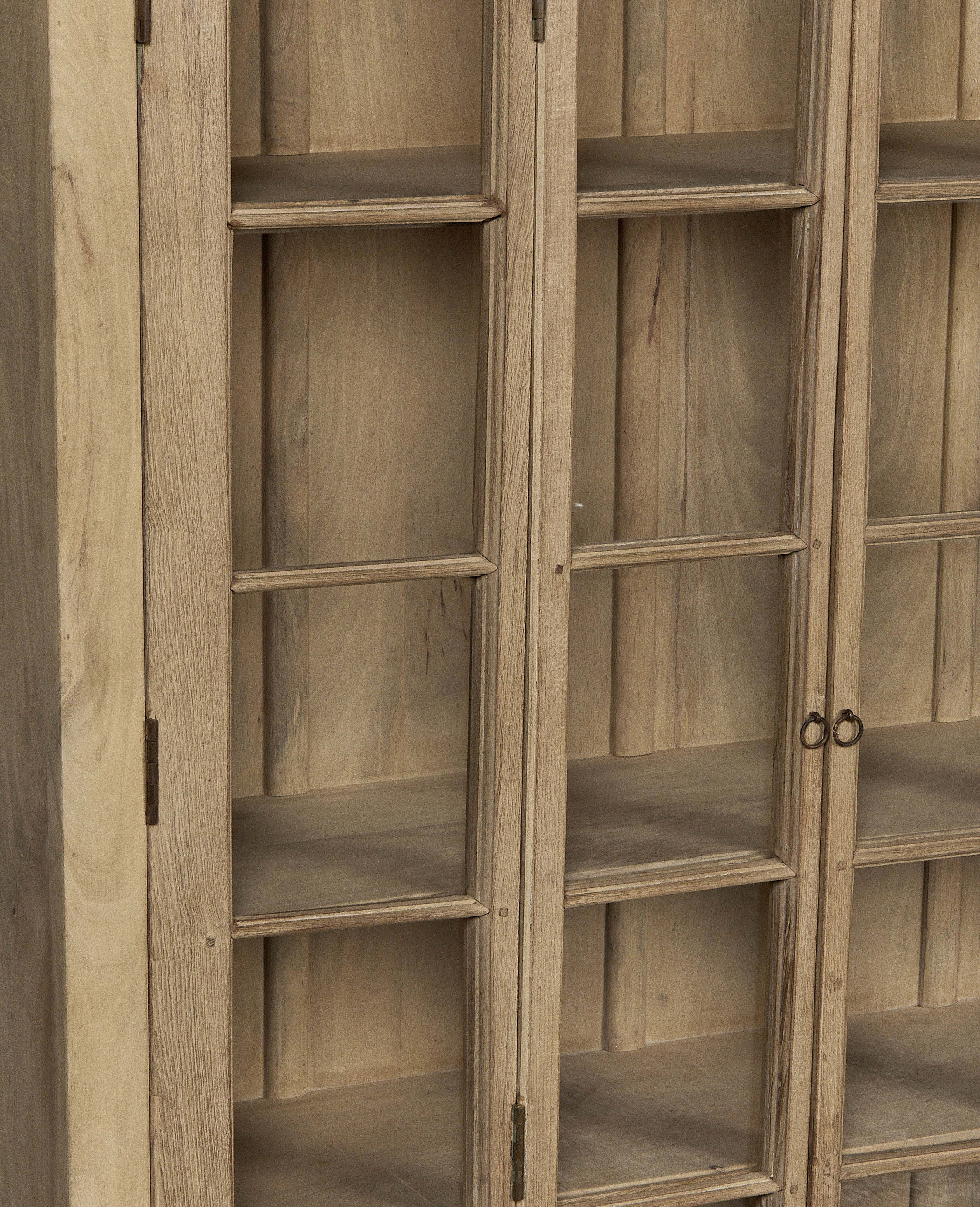 Close-up of vintage bleached oak wood cabinet doors, showing glass panes and antique metal hinges.