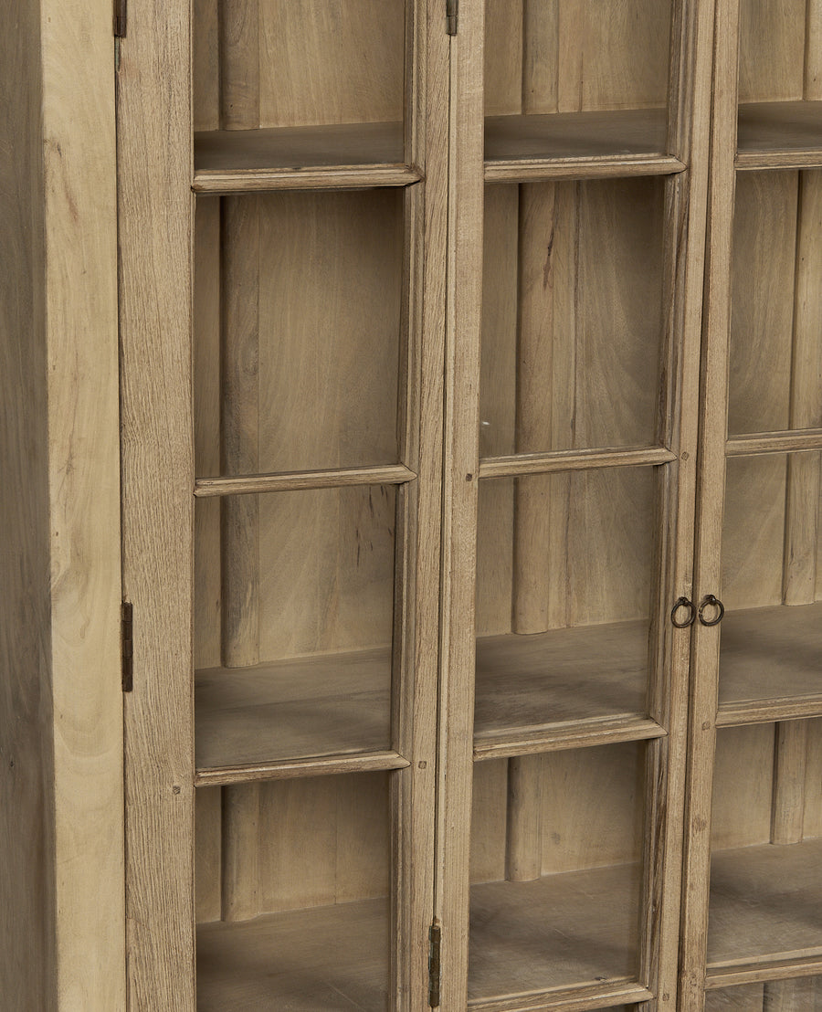 Close-up of vintage bleached oak wood cabinet doors, showing glass panes and antique metal hinges.