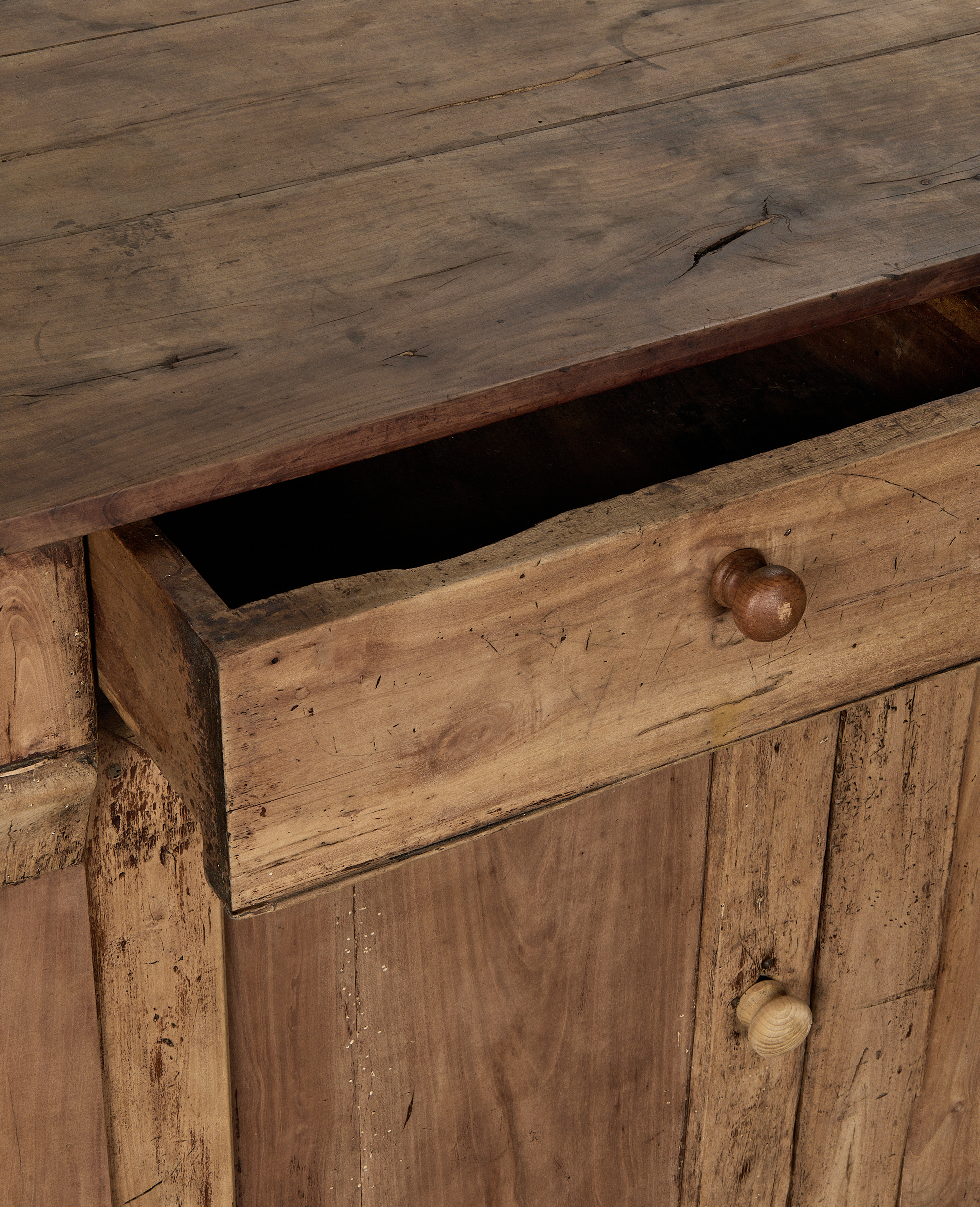 Open drawer on vintage French oak sideboard, revealing distressed wood grain and knob details.