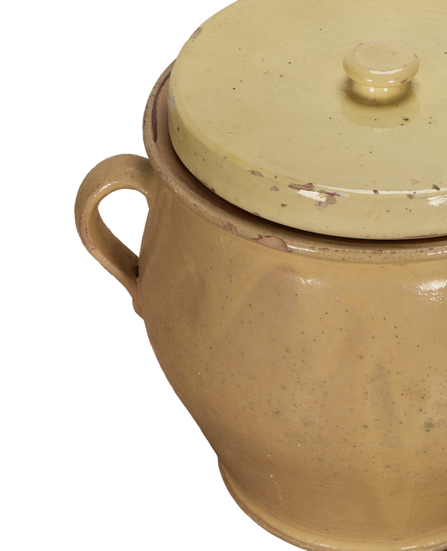 Close-up of antique French confit pot's yellow glazed lid with chipped rim and handle.