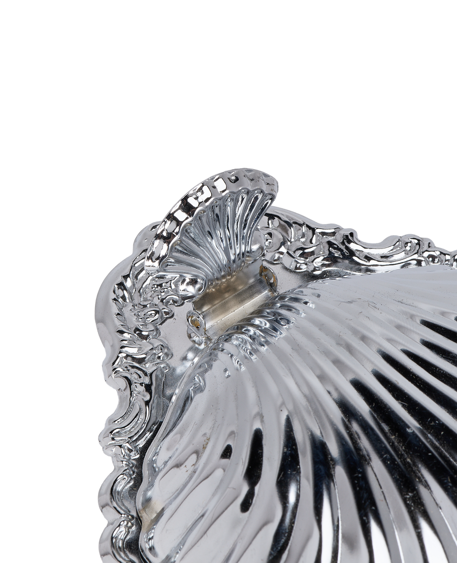 Close-up of vintage French steel butter dish hinge, showing ornate shell and scrolled details.