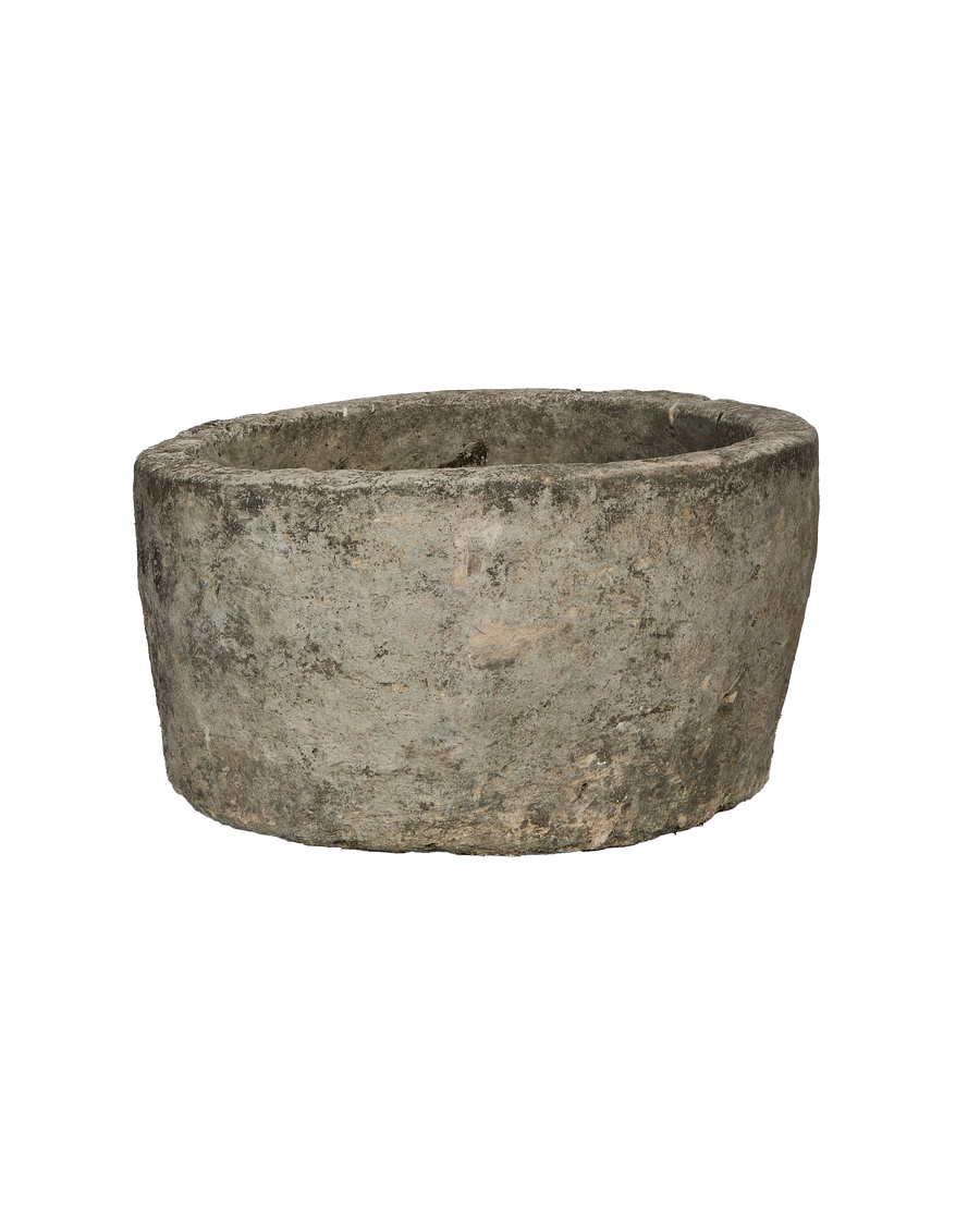 Vintage round, rough-textured Indonesian limestone trough showing weathered exterior from side angle.